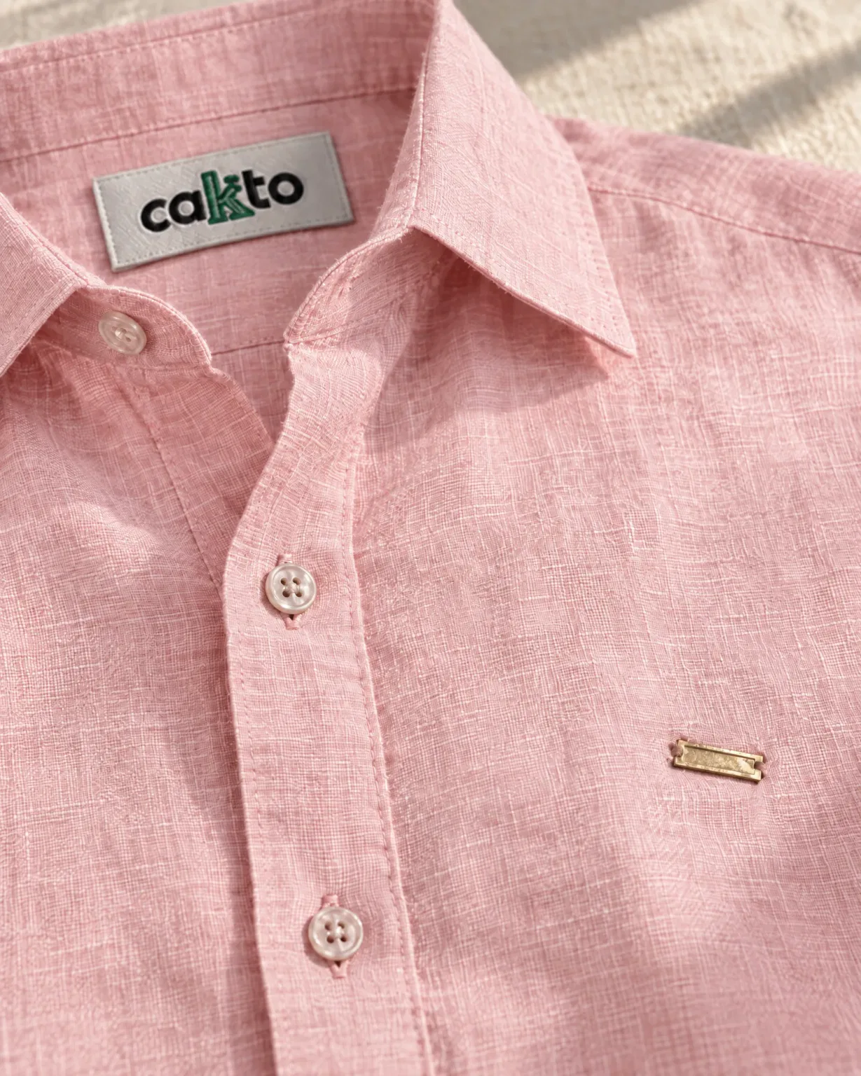 Detalle de la tela, la plaquita metálica y la etiqueta Cakto de la camisa 100% lino rosada