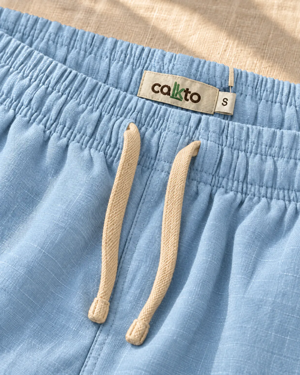 Detalle de la pretina con cordón y marquilla Cakto de la bermuda de lino azul claro