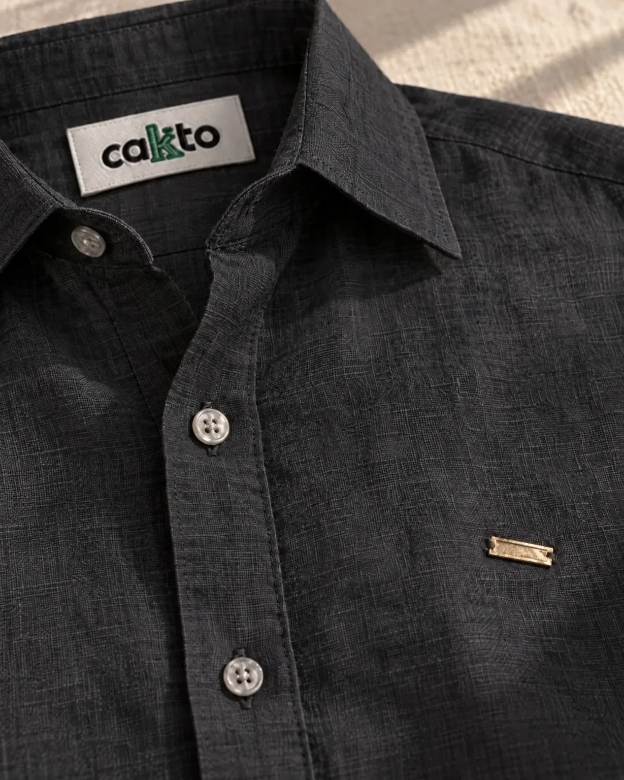 Detalle de la tela, la plaquita metálica y la etiqueta Cakto de la camisa 100% lino negra