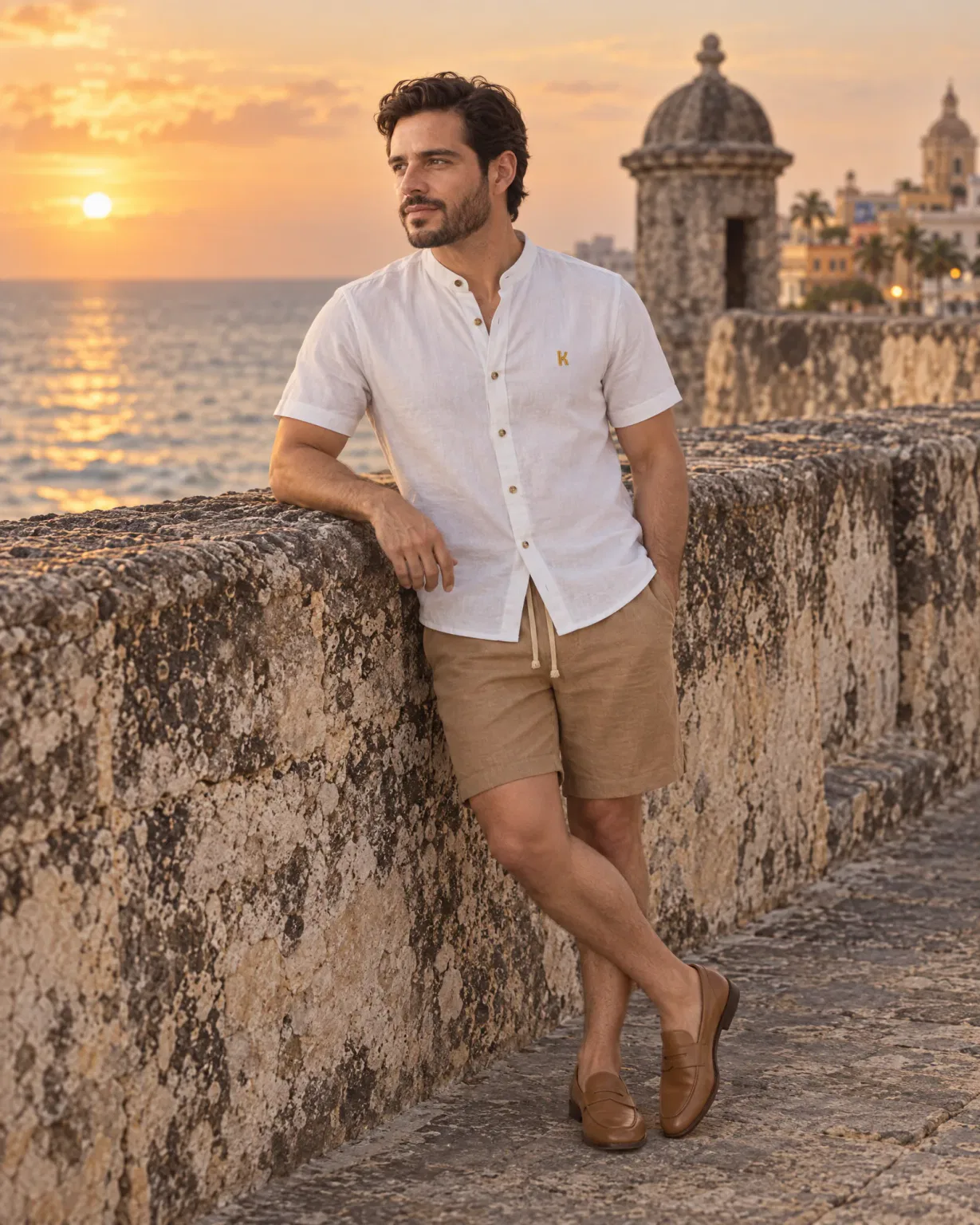 Hombre con camisa cuello neru blanca con bermuda de lino café en las murallas de Cartagena al atardecer