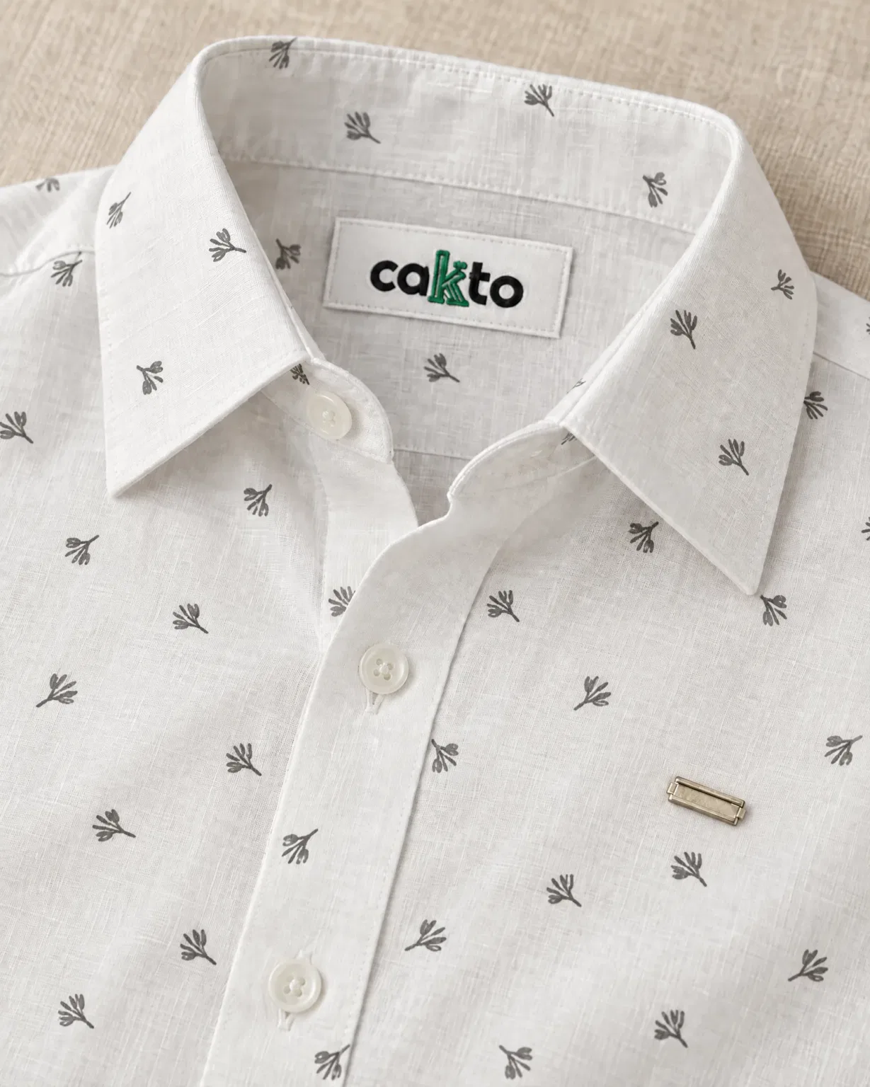 Detalle del estampado de espigas, la plaquita y la etiqueta Cakto de la camisa trigo blanca