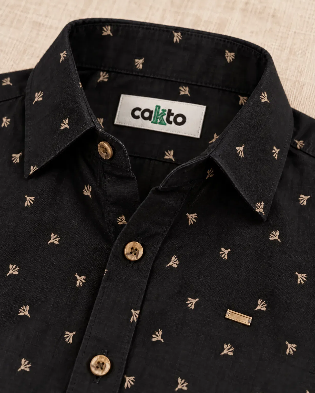 Detalle del estampado de espigas, la plaquita y la etiqueta Cakto de la camisa trigo dorado negra
