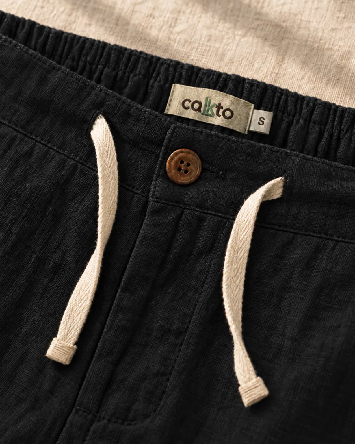 Detalle de la pretina con botón, cordón y marquilla Cakto del pantalón de lino negro